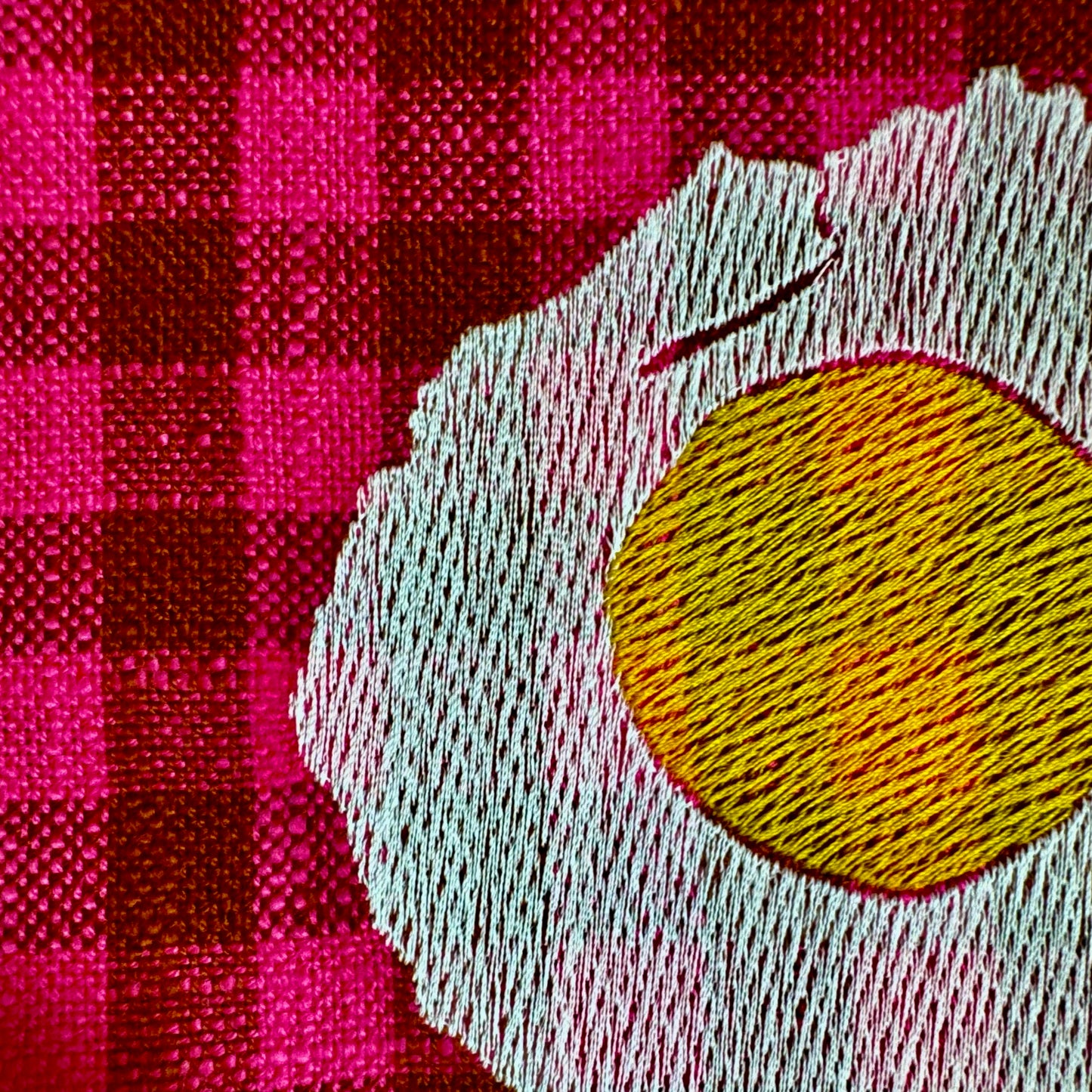 Macro view of machine embroidery stitching on the sunny-side-up egg design showing thread texture