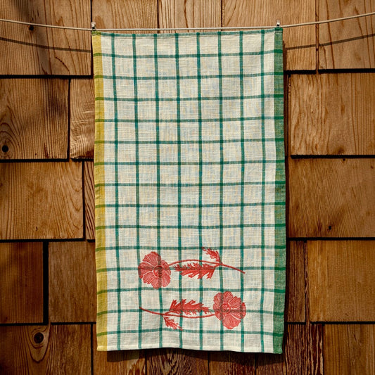 Full-length view of cream and turquoise windowpane plaid tea towel with embroidered orange poppies near the bottom hem