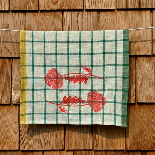 Cream and turquoise windowpane plaid tea towel with embroidered orange poppies, hanging on a clothesline