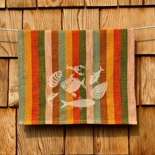 Multicolor striped cotton tea towel with cream embroidered fish and shell design, hanging on a clothesline