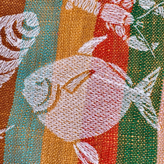 Close-up of hand-drawn fish, shell, and crab embroidery in cream thread on striped cotton tea towel