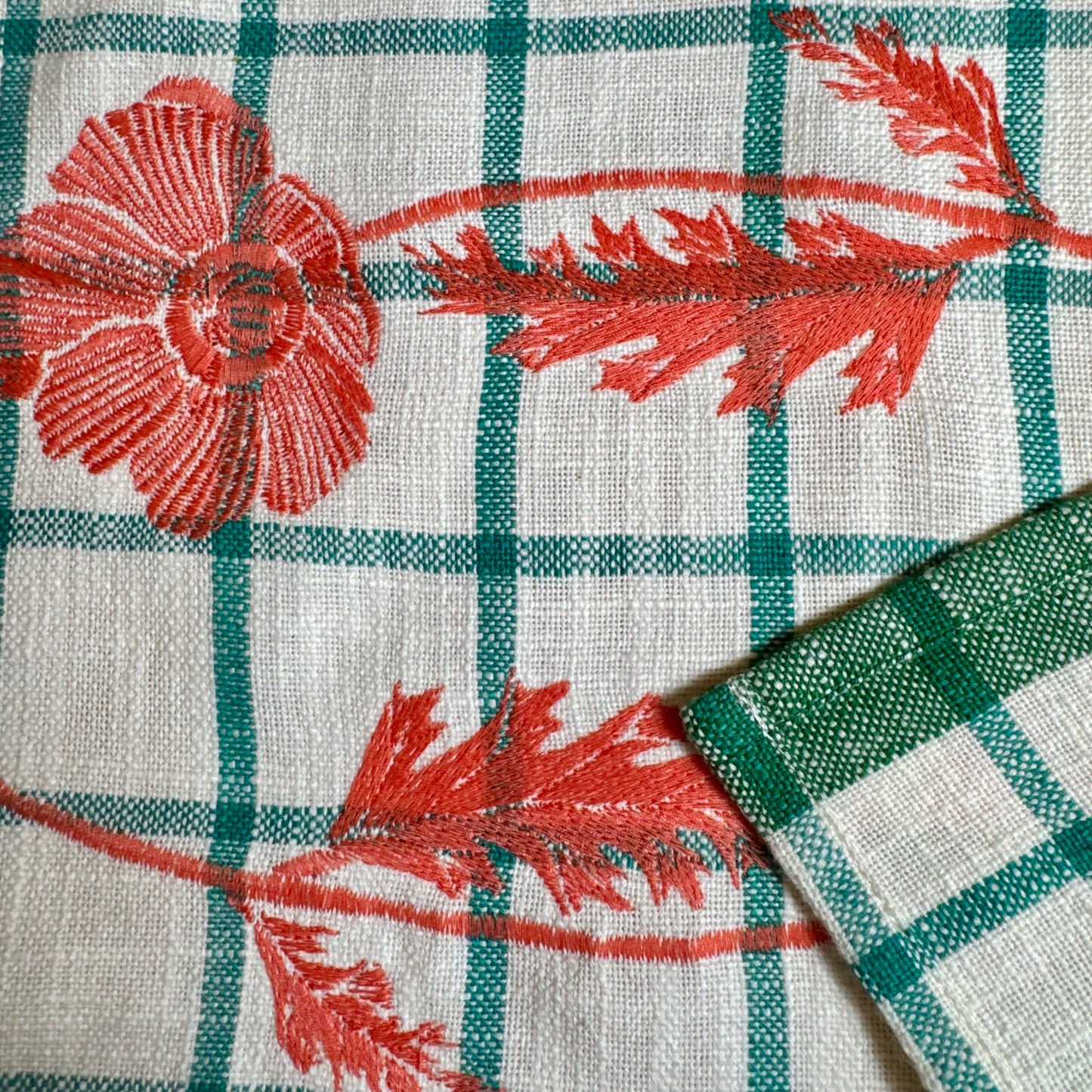 Macro view of orange poppy embroidery stitching detail with green selvedge edge on tea towel hem