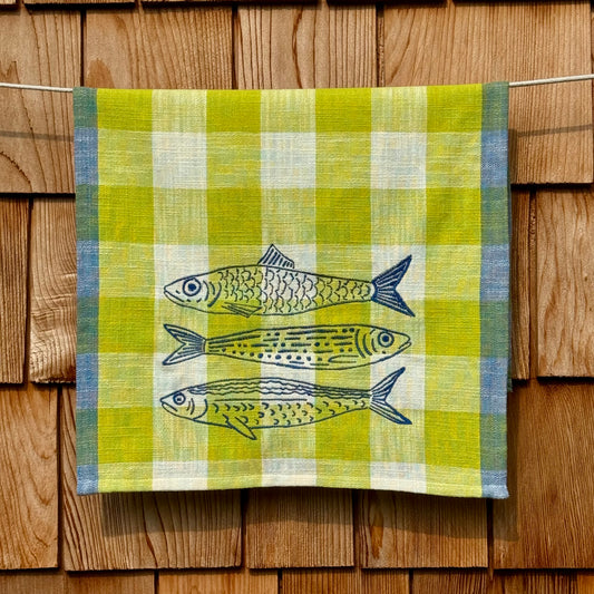 Citron, cream, and blue plaid cotton tea towel with three hand-embroidered fish, hanging on a clothesline