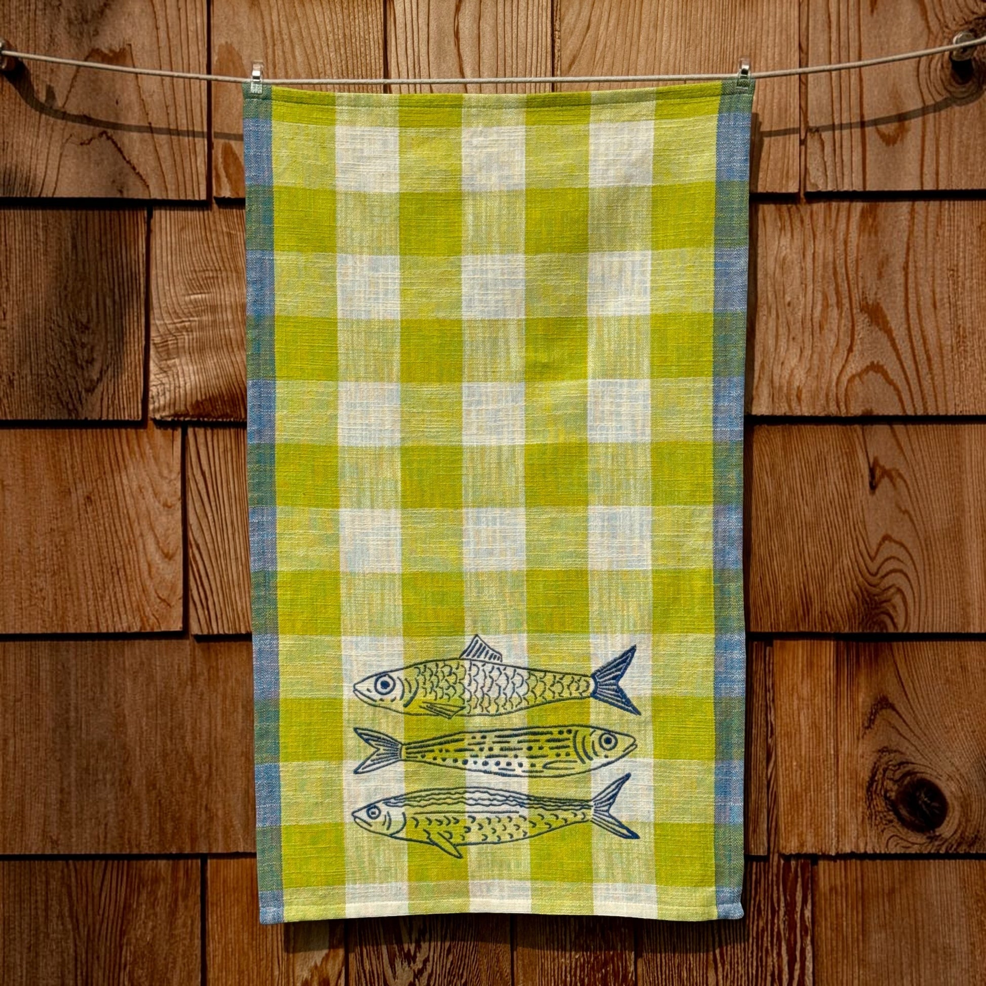 Full-length view of citron and blue plaid tea towel with three embroidered fish near the bottom hem