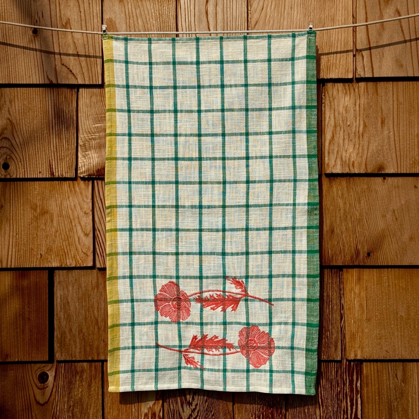 Full-length view of cream and turquoise windowpane plaid tea towel with embroidered orange poppies near the bottom hem